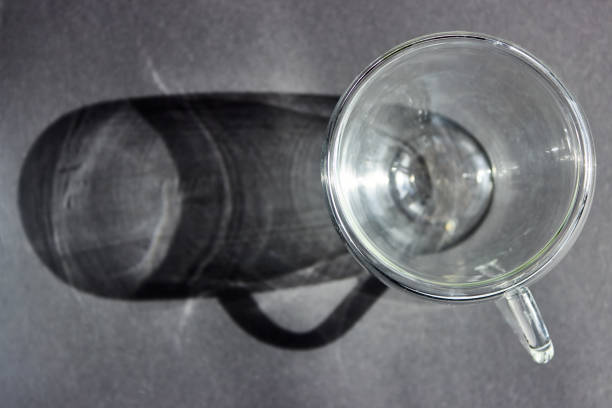 A long gray shadow from a transparent glass cup. Dark gray abstract background for design, social networks with space for text. Top view.