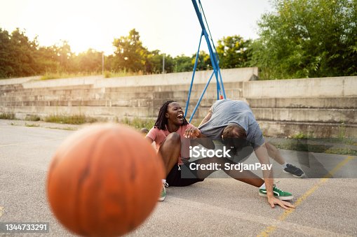 istock Multiracial couple having a laugh after they felt down during pick-up basketball game 1344733291