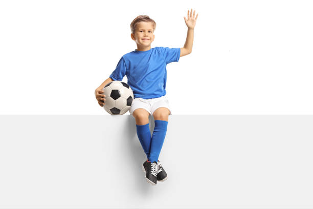 istock Child waving and sitting on a blank panel with a soccer ball 1344733339