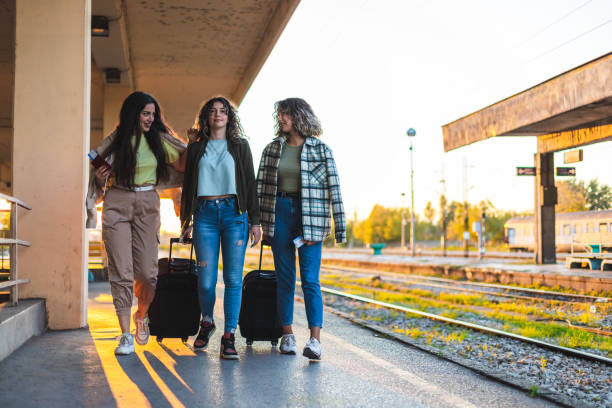 istock Three beautiful young female friends walking at a train station with two suitcases during sunset while waiting to travel by train 1344739109