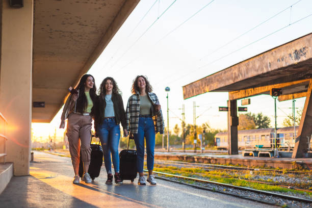 istock Three beautiful young female friends walking at a train station with two suitcases during sunset while waiting to travel by train 1344739111