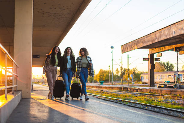 istock Three beautiful young female friends walking at a train station with two suitcases during sunset while waiting to travel by train 1344739121