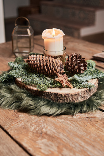 centro de mesa navideño de estilo rústico con una vela encendida y piñas sobre una mesa de madera, una vela al fondo. concepto de decoración navideña y advent photo