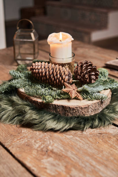 rustic style christmas centerpiece with a lit candle and pinecones on a wooden table, a candle in the background. concept christmas and advent decoration - pronkstuk stockfoto's en -beelden