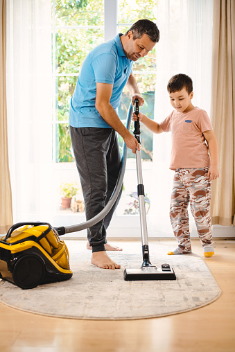 Father and son sweeping the house with a vacuum cleaner at home