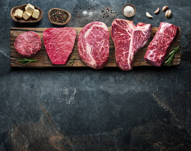istock Different raw beef steaks on the wooden board on the grey table. Top view. 1344743411