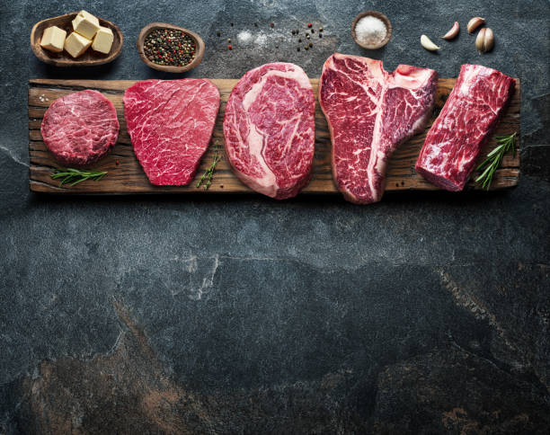 Different raw beef steaks on the wooden board on the grey table. Top view. stock photo