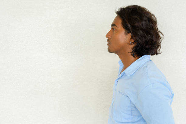 Profile view shot of handsome young Indian man against plain background outdoors shot with natural light