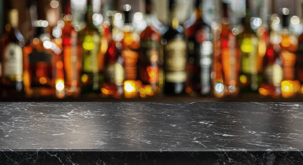 graue tischplatte und schöne bokeh-regale mit alkoholflaschen im hintergrund. bar-konzept. - alcohol stock-fotos und bilder