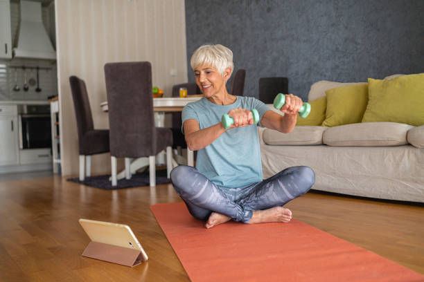 istock Cheerful and active senior woman, following online exercising tutorial while doing the home workout with dumbbells 1344744098