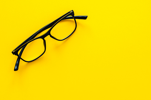 Black modern eyeglasses shot from above on yellow background. The composition is at the top left of an horizontal frame leaving useful copy space for text and/or logo at the right. High resolution 42Mp studio digital capture taken with Sony A7rII and Sony FE 90mm f2.8 macro G OSS lens