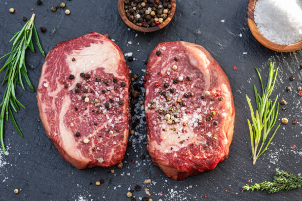 istock Raw Ribeye steaks with salt and herbs on grey board. Top view. 1344745214