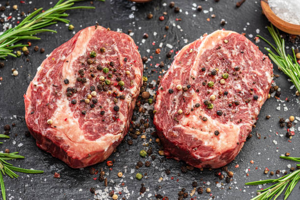 istock Raw Ribeye steaks with salt and herbs on grey board. Top view. 1344745247