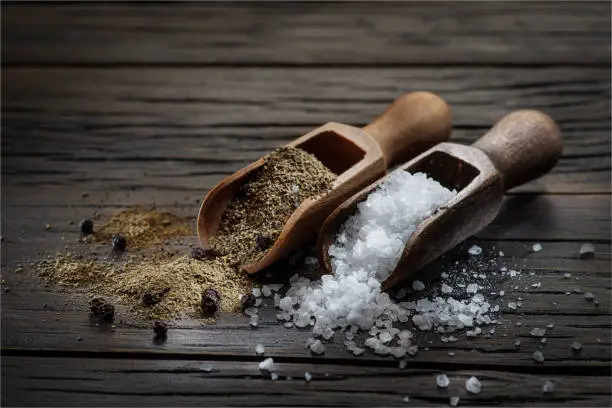 Photo of Sea salt and ground pepper in the wooden spoons on old wooden background. Two most popular ingredients that you put into food.