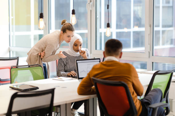 istock Creative team of young individuals working on desktop and laptop computers in a modern office space.. 1344747873