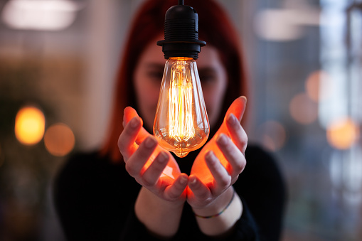 Portrait of a beautiful business woman with red hair in front of a decorative light bulb.