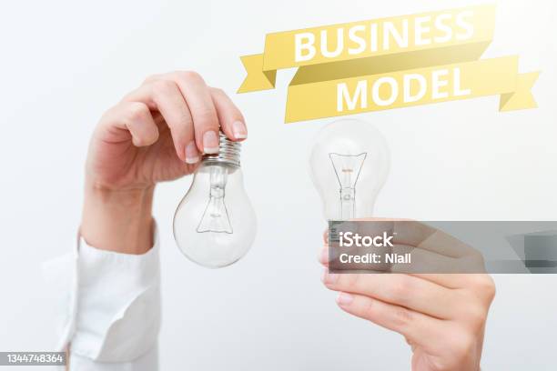 Hand Writing Sign Business Model Word Written On Strategy That A Company Uses To Generate Revenue Or Profit Two Hands Holding Lamp Showing Or Presenting New Technology Ideas Stock Photo - Download Image Now