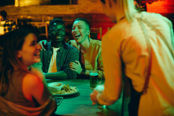 istock Group of young people having fun and laughing while waitress is serving them drinks in a pub. 1344748421