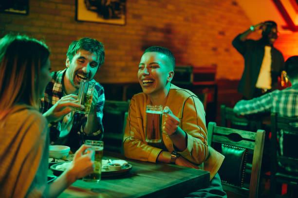 istock Young cheerful people drinking beer and talking in a pub at night. 1344748675