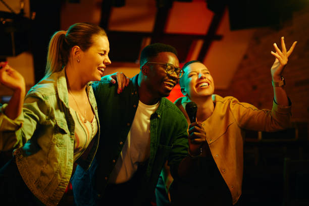 African American man and his female friends singing karaoke and having fun during their night out in a bar. Young happy people singing on karaoke party in a out at night. Focus is on African American man. karaoke stock pictures, royalty-free photos & images