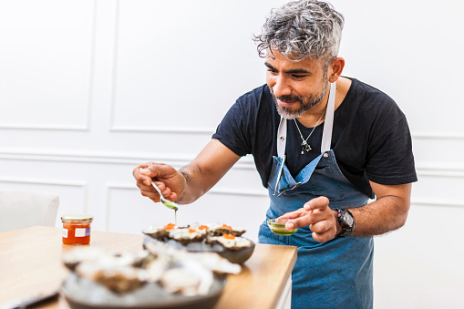 Latin cook cooking oysters with trout roe and coriander oil. Chef preparing food for a private dinner at home.