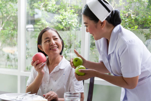 간호사 돌보는 또는 집에서 사과 또는 과일을 먹는 고위 아시아 여성을 추천합니다. 간호사 조수 주의 노인 아시아 여자와 친절. 은퇴, 건강 관리 및 노화 개념 - senior adult nursing home eating home interior 뉴스 사진 이미지