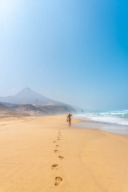 A young tourist walking alone on the wild beach Cofete in the natural park of Jandia, Barlovento coast, south of Fuerteventura, Canary Islands. Spain stock photo