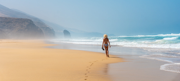 Panorámica de un joven turista con sombrero caminando solo por la playa de Cofete del parque natural de Jandía, Barlovento, al sur de Fuerteventura, Islas Canarias. España photo