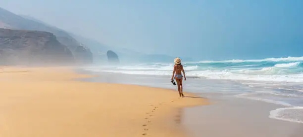 Panoramic of a young tourist with a hat walking alone on the Cofete beach of the Jandia natural park, Barlovento, south of Fuerteventura, Canary Islands. Spain