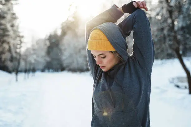 Young athletic woman warming up before her winter workout during sunny and snowy day