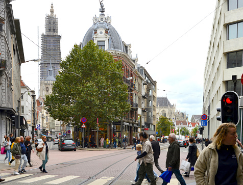 Antwerp Belgium - October 2, 2021:  People cross the street at a green traffic light in front of a tree and the corner house at 16 National street in Antwerp, one of Dries Van Noten's real estate fashion houses that sold his brand empire to Spanish clothing brand Puig.