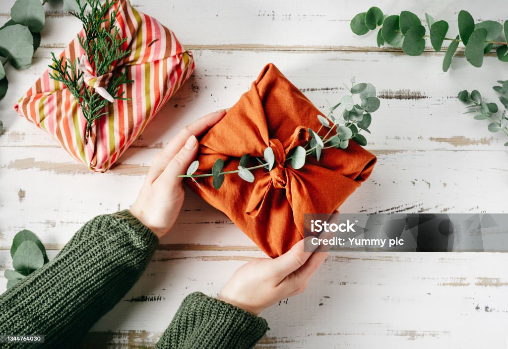 Wrapping a gift in eco friendly reusable fabric package furoshiki Furoshiki tissue wrapping of presents. Female hand holding a gift in eco friendly reusable fabric package. Small business, ethical shopping idea. Presents packed in plastic free. Zero waste lifestyle Gift Stock Photo