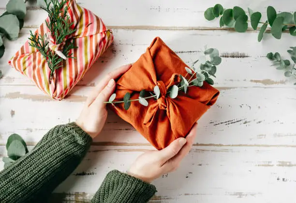 Furoshiki tissue wrapping of presents. Female hand holding a gift in eco friendly reusable fabric package. Small business, ethical shopping idea. Presents packed in plastic free. Zero waste lifestyle