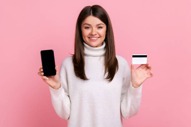 istock Smiling optimistic female holding credit card and smart phone with empty display for advertisement. 1344765150