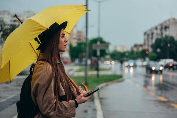 istock Woman using a smartphone and holding yellow umbrella while in the city while it rains 1344765574