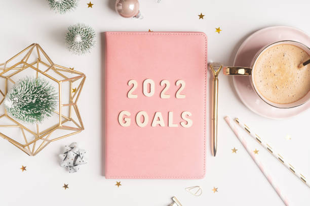 istock Top view Desktop Christmas pink notepad with 2021goals letters text. Flat lay of white table background with planner, cup of coffee, Christmas decoration, notebook and stationery 1344765756