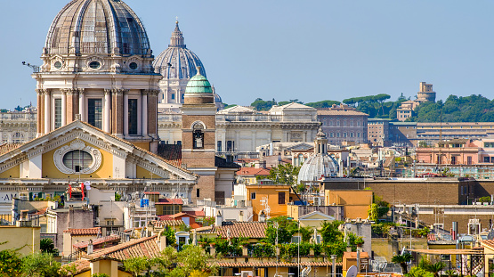 The suggestive and detailed view over the rooftops of Rome from the terrace of the monumental staircase of Trinità dei Monti, better known as Spanish Steps, in the historic and baroque heart of the Eternal City. In the foreground the dome of the Basilica of Santi Ambrogio e Carlo, along Via del Corso, behind the majestic dome of St. Peter's Basilica on the horizon. In 1980 the historic center of Rome was declared a World Heritage Site by Unesco. Image in 16:9 and high definition format.