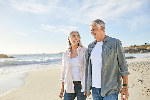 Smiling couple walking at beach on sunny day. Mature man and woman are on summer vacation. They are wearing casuals.