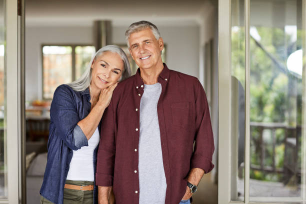 Smiling mature couple at home during lockdown Portrait of smiling mature man and woman. Couple is spending leisure time at home during COVID-19 lockdown. They are wearing casuals. 55 59 years stock pictures, royalty-free photos & images