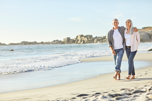 Happy couple walking at beach on sunny day. Mature man and woman are enjoying summer vacation. They are at seashore.