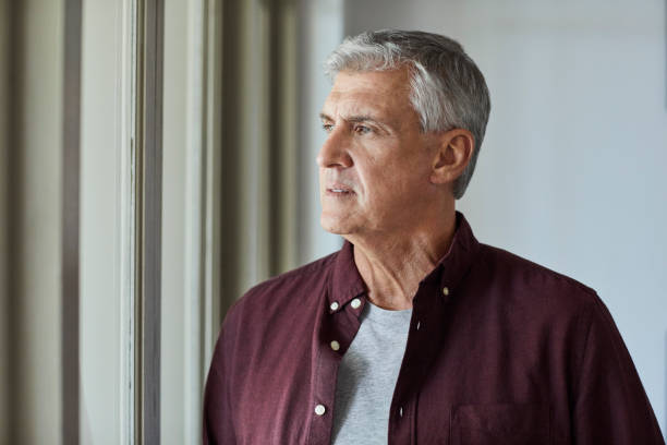 istock Thoughtful man looking through window at home 1344767818