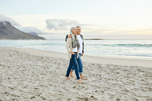 Mature couple walking at sandy beach. Man and woman are enjoying vacation. They are at seashore during sunset.