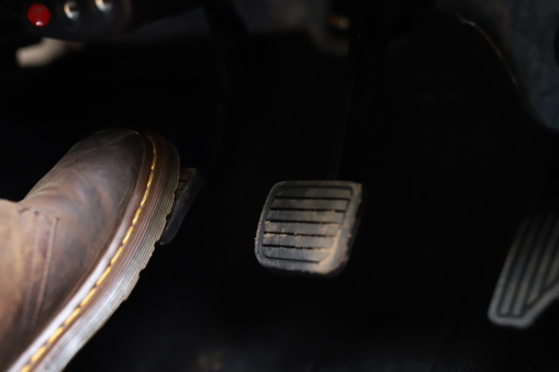 Foot and accelerator and brake pedal inside the car or vehicle. and copy the area that the brown leather boots step on to increase the speed or control the stride of the car. car driving concept