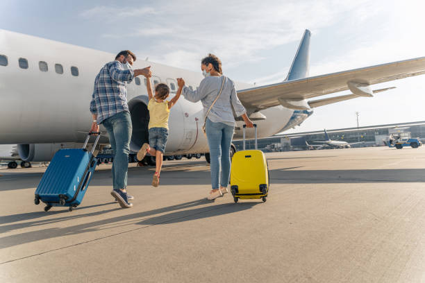 Happy family in masks enjoying travel together Back view of parents holding the hands of the child and going with suitcases to board the plane airport stock pictures, royalty-free photos & images