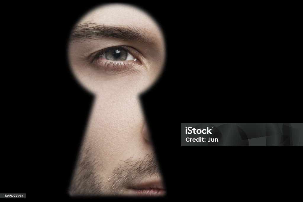 Male eye looking into the keyhole Closeup of male eye looking into the keyhole Surveillance Stock Photo
