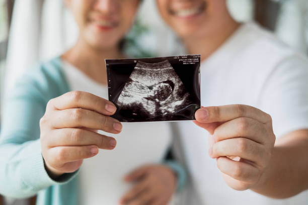 pareja de embarazadas asiáticas que se siente feliz muestra una imagen de ultrasonido en casa, concéntrese en la imagen de ultrasonido - pareja joven fotos fotografías e imágenes de stock