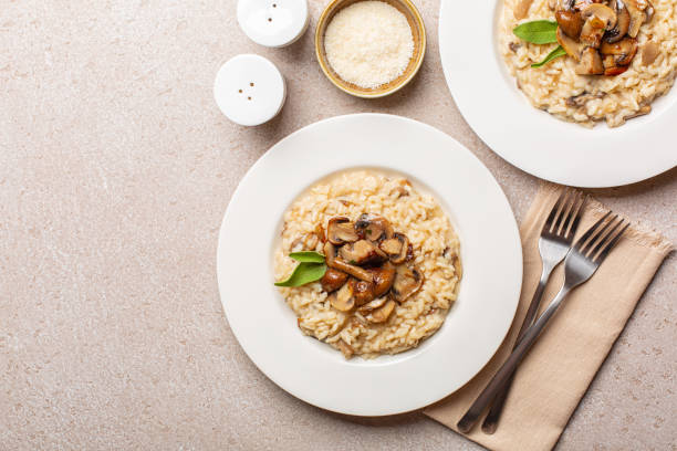 Risotto with mix of mushroom and taleggio cheese on stone beige table. Two portions. Top view. Copy space. stock photo