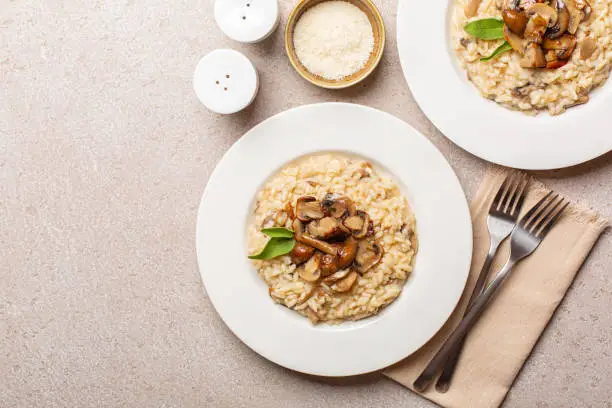 Risotto with mix of mushroom and taleggio cheese on stone beige table. Two portions. Top view. Copy space.