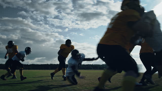 American Football Field Two Teams Compete: Players Pass and Run Attacking to Score Touchdown Points. Athletes Brutally Compete for the Ball, Tackle Each other. Cinematic Slow Motion with Dramatic Shot
