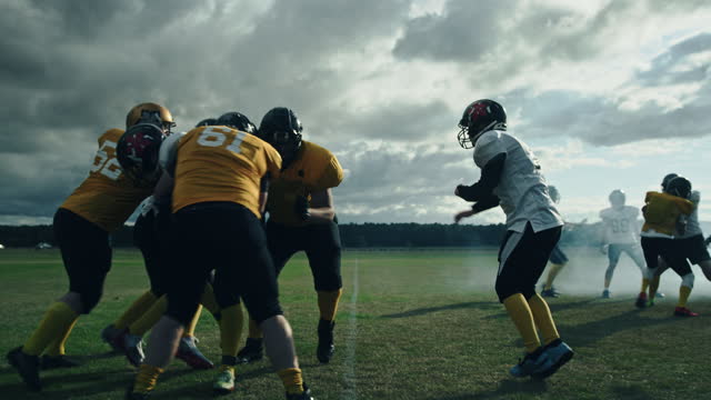American Football Field: Two Professional Teams Clash, Attacking to Score Touchdown Points. Athletes Brutally Compete for the Ball, Tackle Each other. Dramatic Slow Motion with Immersive Cinematic
